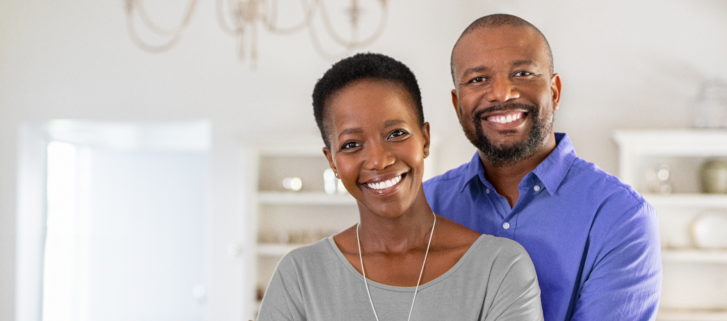 Foto de um casal abraçado sorrindo. Os dois têm idade por volta de 40 e poucos anos. A mulher é negra, tem cabelos curtos e veste uma blusa azul claro. O homem é negro, tem cabelos raspados, barba rala e veste uma camisa azul. Do lado esquerdo da foto, há o texto “Plano Alfa Pro. Nunca é tarde pra ter o sorriso dos seus sonhos. Apenas R$ 161,00 por mês.