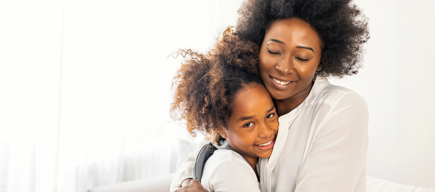 Foto de uma mãe, com idade por volta de 30 e poucos anos, abraçada com a filha, com idade por volta de 10 anos, sorrindo. As duas são negras, têm cabelos crespos e vestem blusas brancas.  Do lado esquerdo da foto, há o texto “Plano Alfa. Boca saudável sem choro nem ranger de dentes. Apenas R$ 65,90 por mês